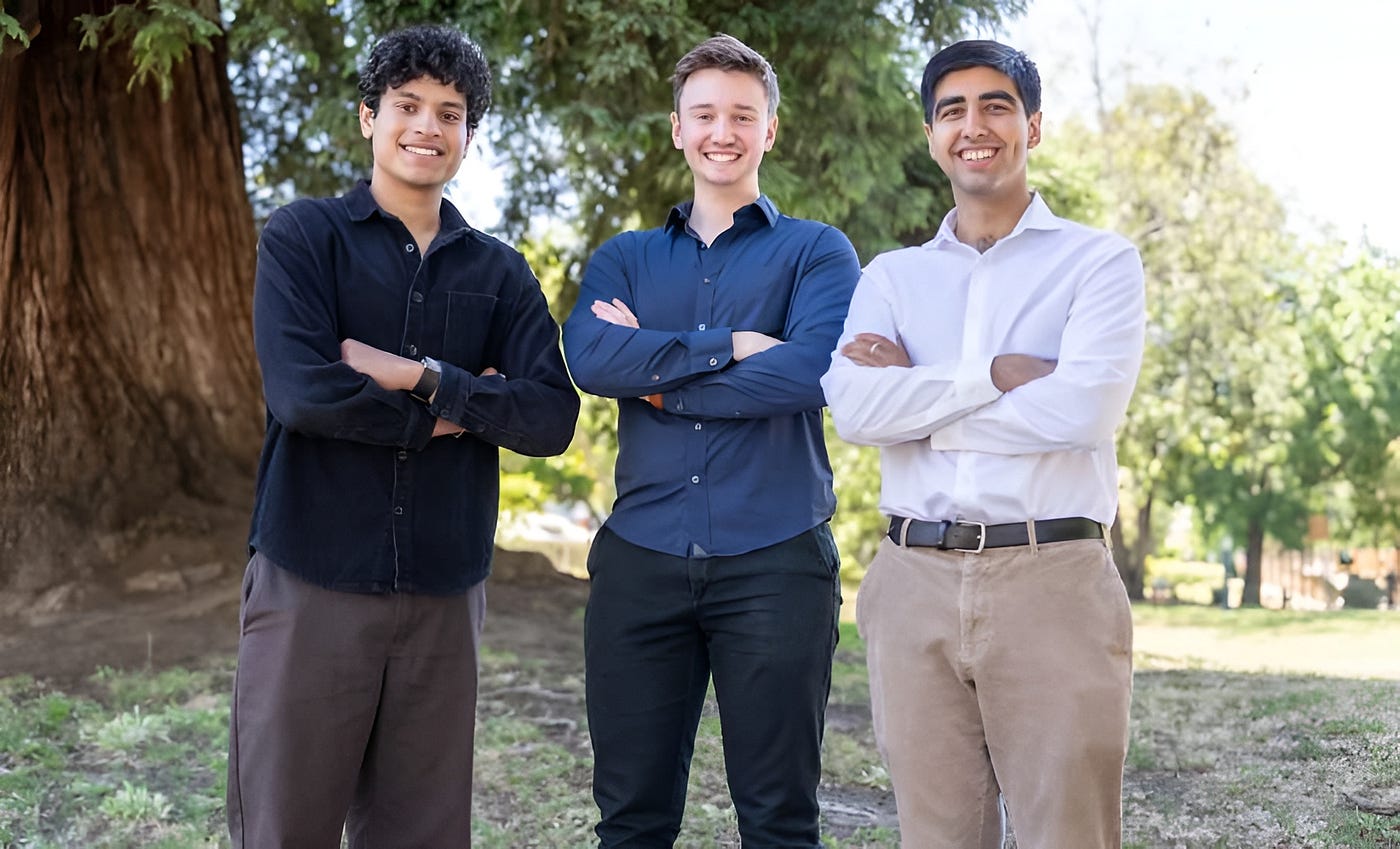 Three young entrepreneurs standing outdoors with arms crossed, smiling confidently in front of trees on a sunny day.