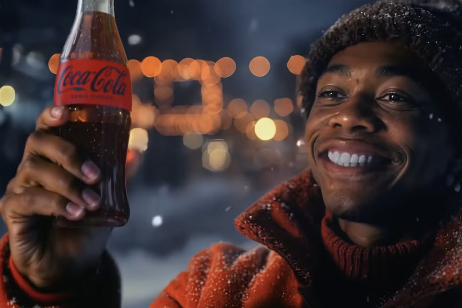 A smiling person in a winter coat holds up a bottle of Coca-Cola in a snowy, warmly lit holiday scene.