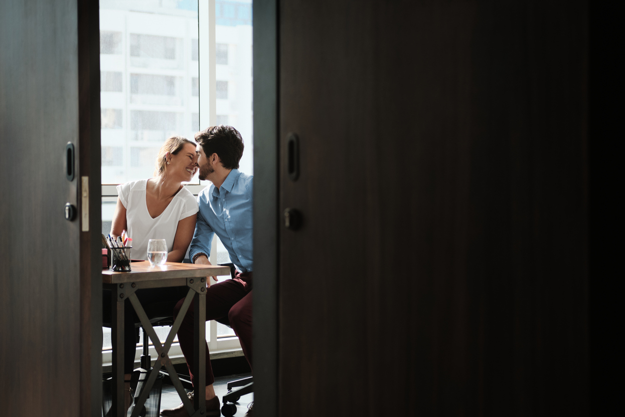 two co workers sitting at office desk and kissing