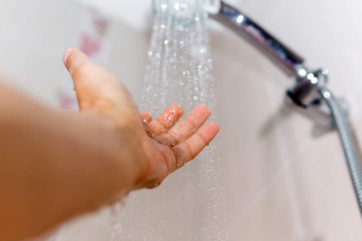 hands check the temperature of the shower water. a man's hand under a stream of water selective focus