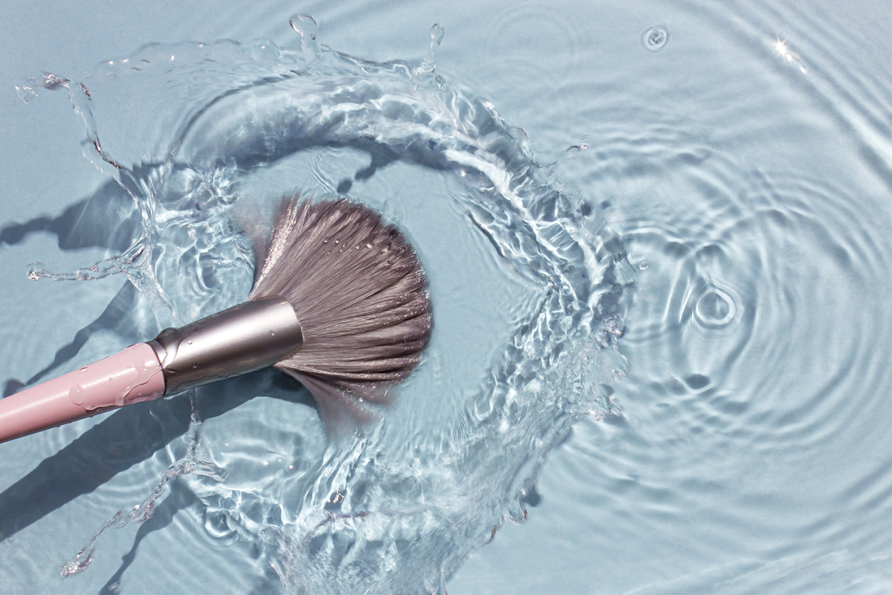 makeup brush in clean water with a splash. summer cosmetics concept.