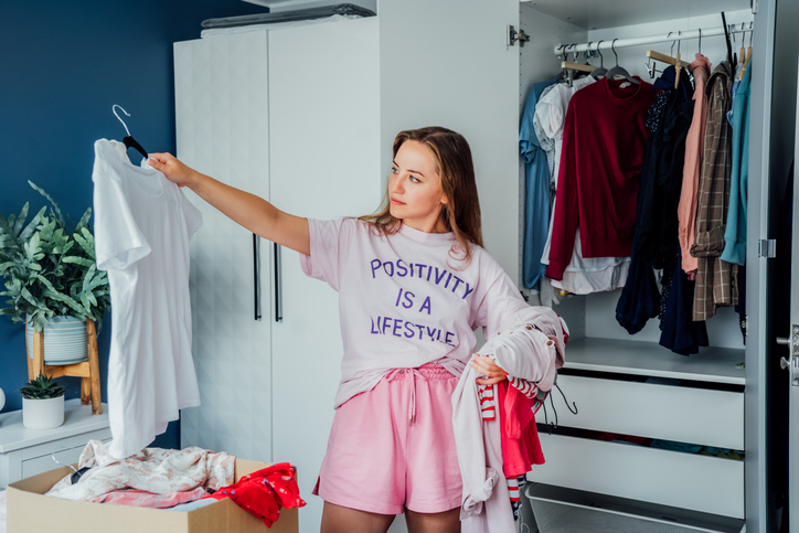 woman selecting clothes from her wardrobe for donating to a charity shop. decluttering, sorting clothes and cleaning up. reuse, second hand concept. conscious consumer, sustainable lifestyle.