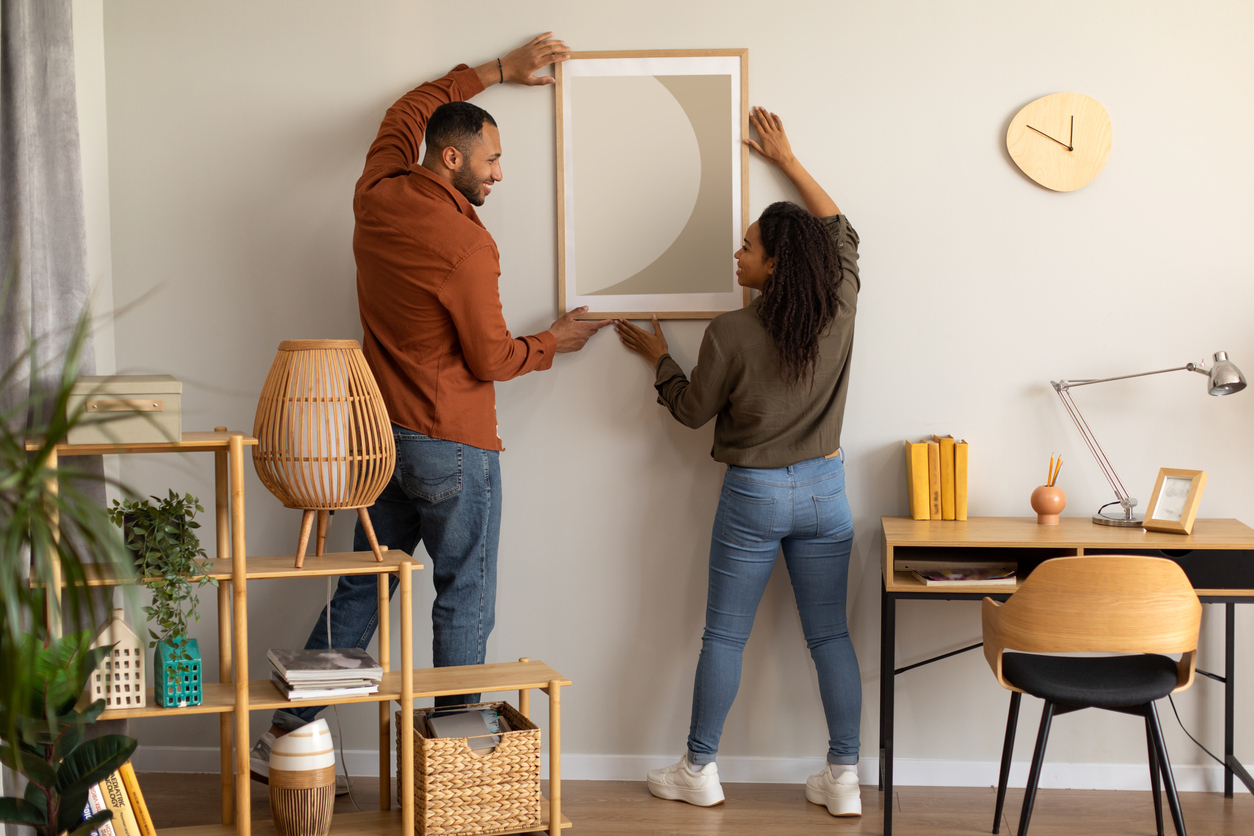 black millennial spouses hanging poster on wall together at home