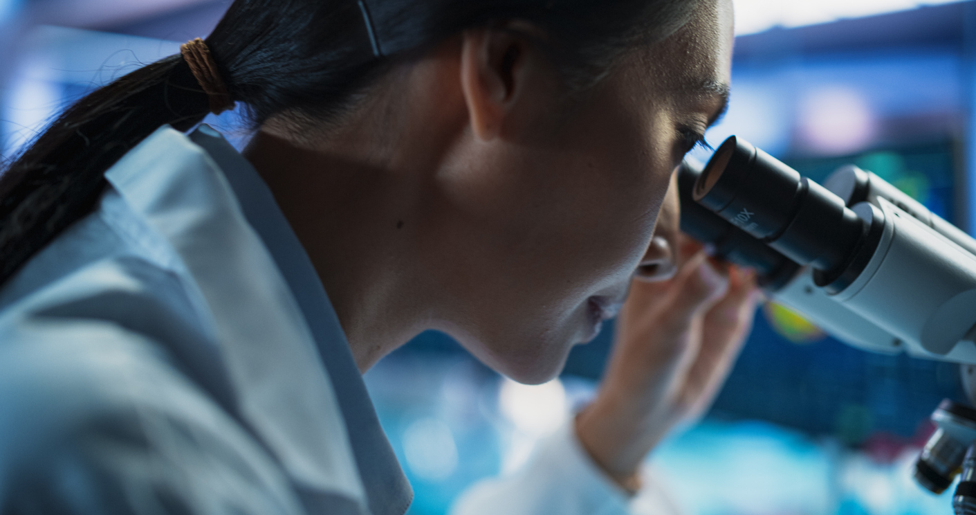 medical development laboratory: close up portrait of asian female scientist using microscope, analyzes petri dish sample. big pharmaceutical lab doing medicine, biotechnology, and drugs research.