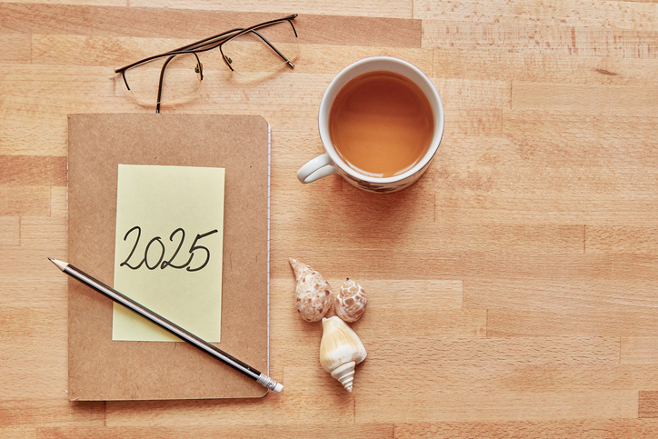 notebook with "2025" sticky note, pencil, and coffee on wooden surface with copy space