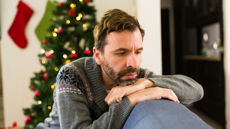 unhappy 30 something man feeling down and blue during the festive season, lounging on a sofa at home