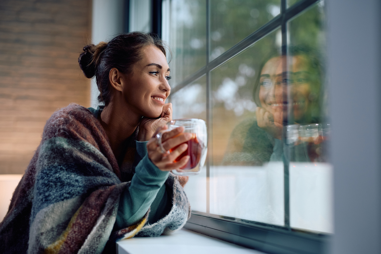 smiling woman day dreaming while drinking warm tea at home.