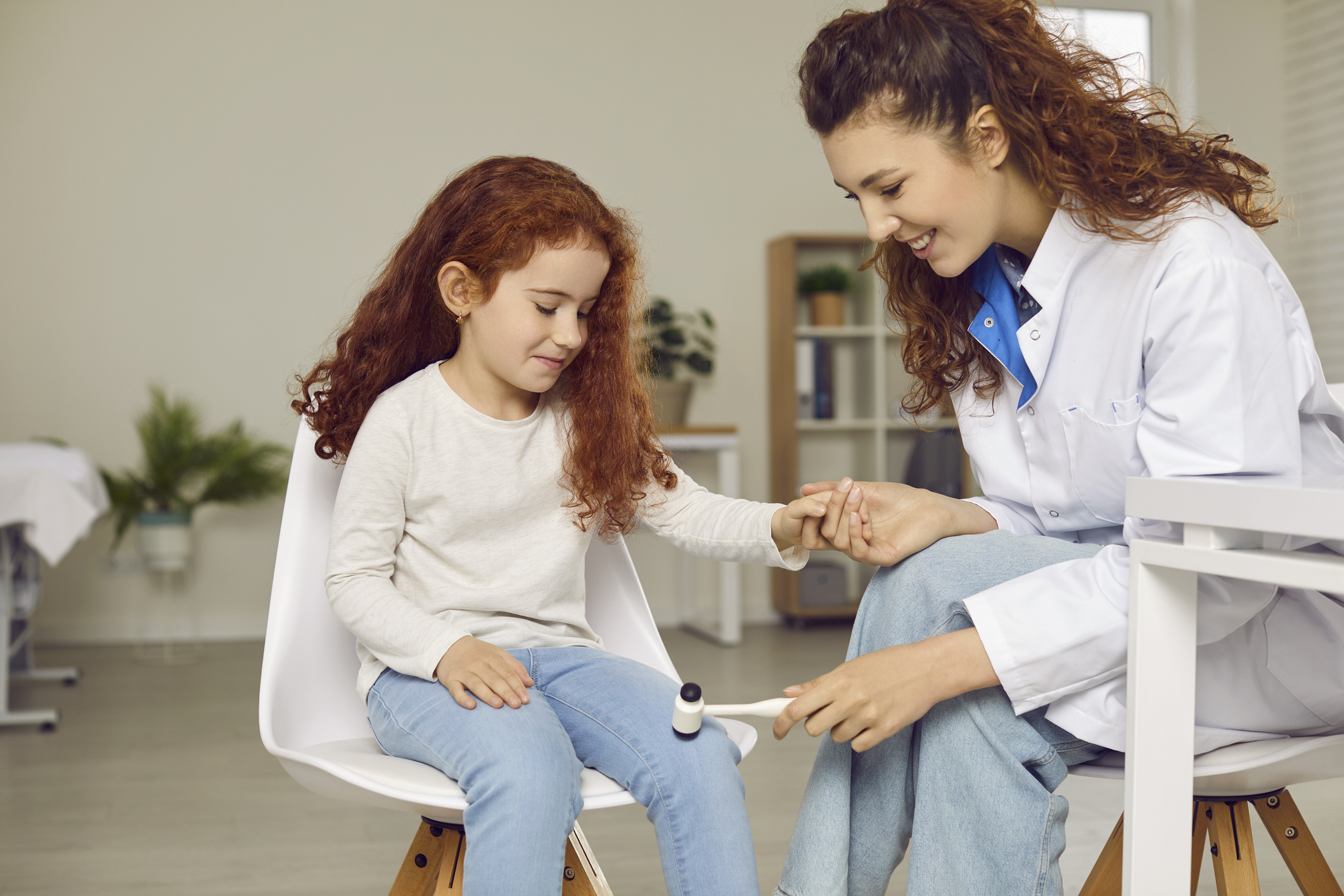 pediatric neurologist examining happy little child and using hammer to test knee reflex