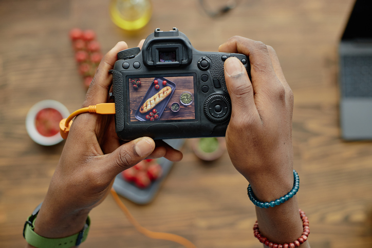 young adult black man photographing pastry with digital camera indoors