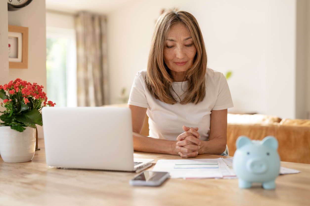 woman sitting at a desk in a cozy living room, focused on financial planning with a laptop and a savings piggy bank in view