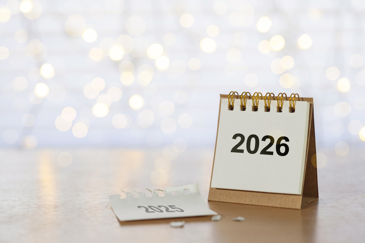 desk calendar turning from 2025 to 2026 on a wooden table with warm bokeh lights, symbolizing year end farewell, new year celebration, resolutions, goals, and fresh beginnings with generous copy space
