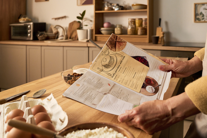 middle aged woman reading recipe book while preparing ingredients