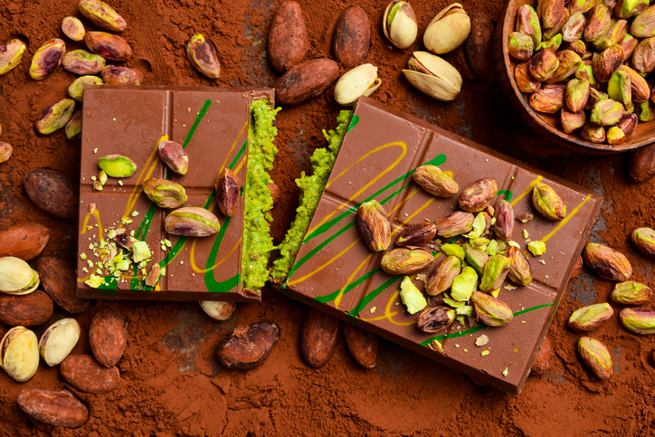 pieces of dubai chocolate bars with pistachios, cocoa beans and knafeh on the table. cocoa powder.