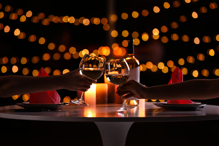 two people toasting with wine glasses at a romantic candlelit dinner table, celebrating an anniversary or valentine's day.