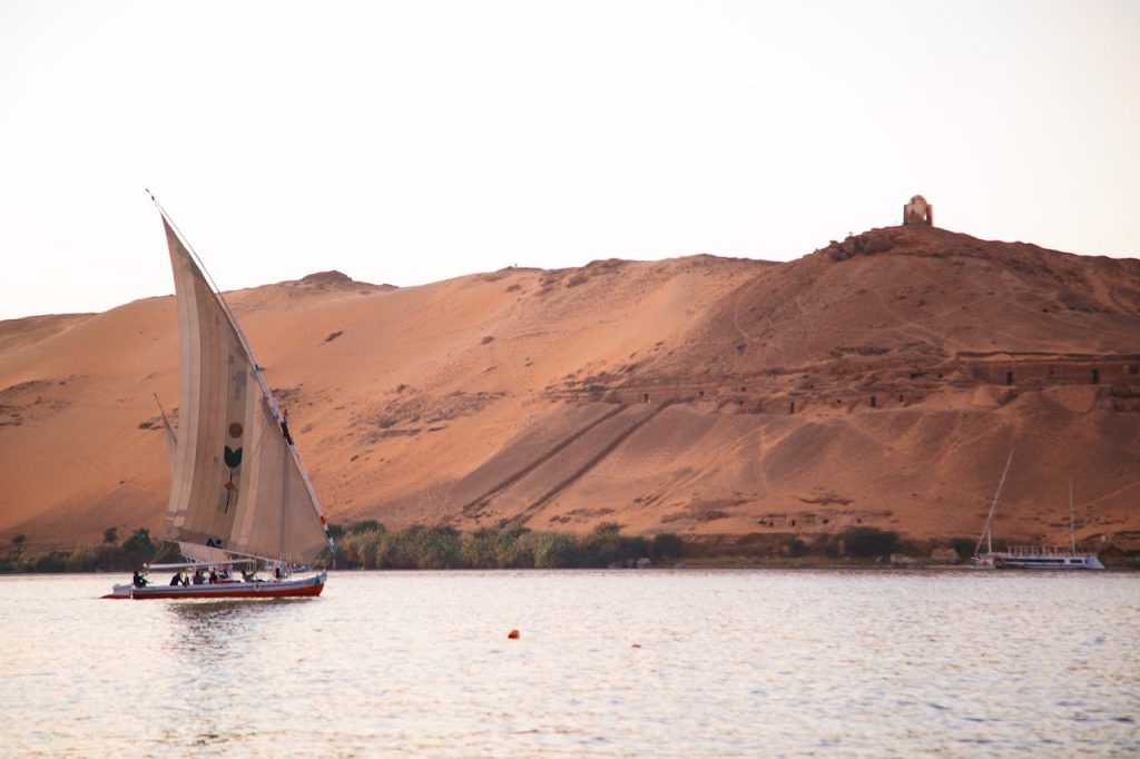 A sail boat is sailing on the water near a sand dune