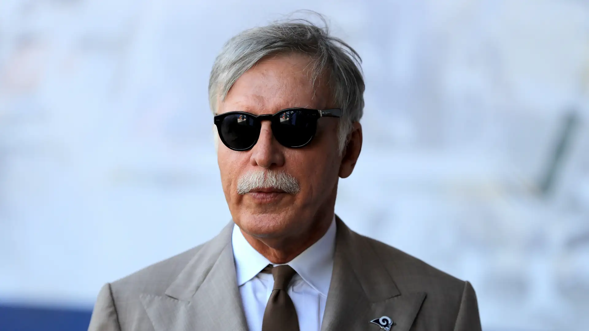 Stanley Kroenke wearing sunglasses and a beige suit at a public sports event