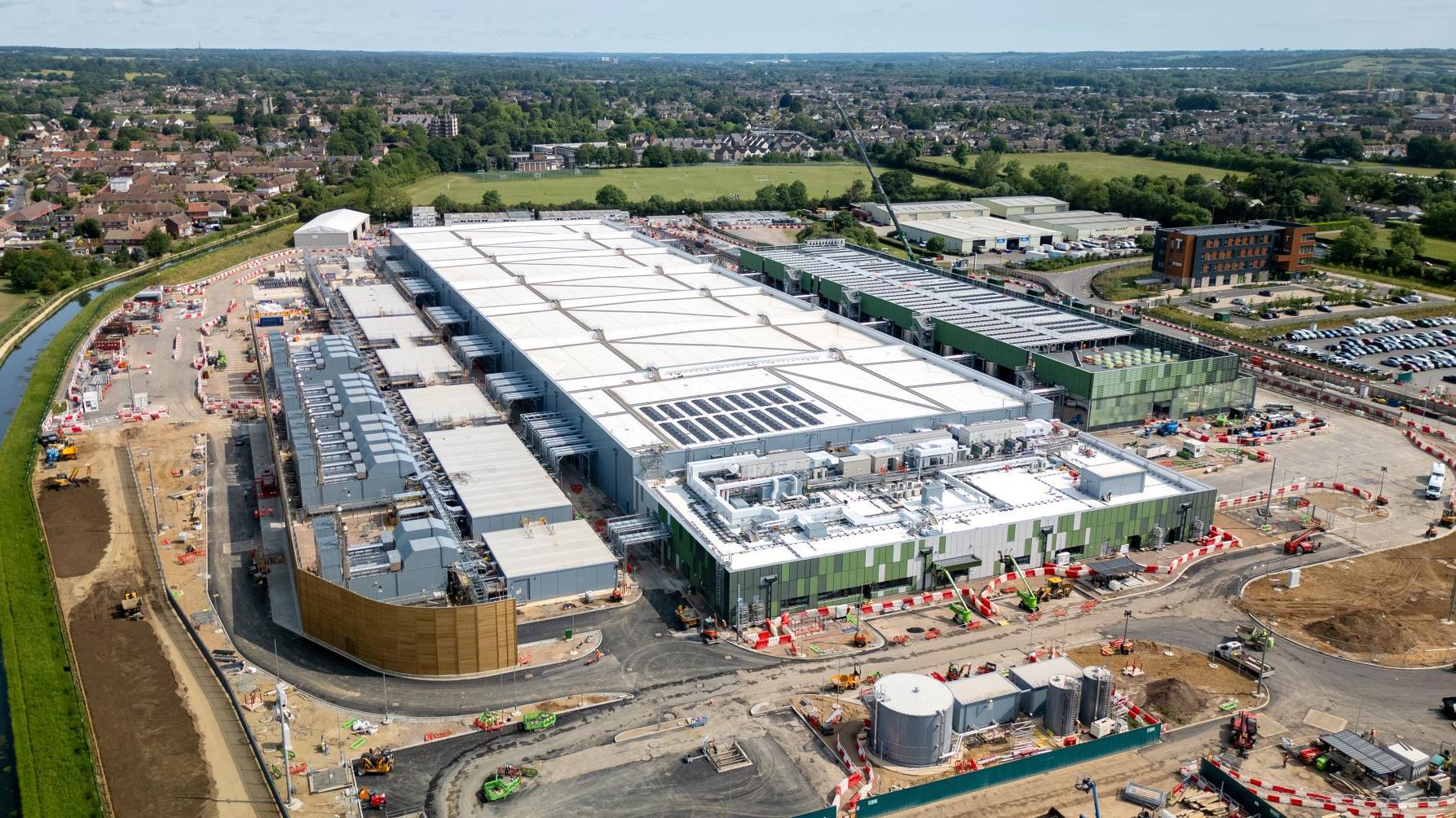 Aerial view of a large-scale data center facility under construction, showing cooling units, power infrastructure, and surrounding development works.