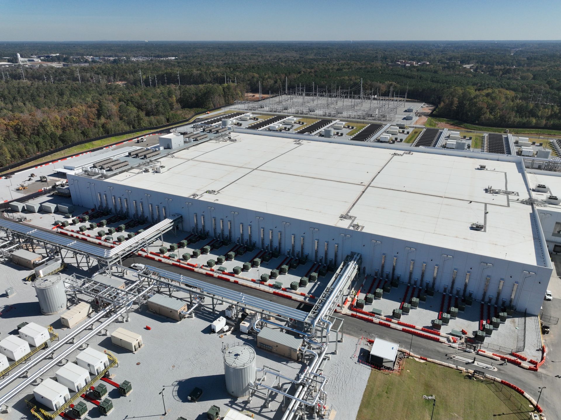 Aerial view of a large AI data center facility with industrial power infrastructure, cooling systems, and a high-voltage substation, showing the scale of modern AI compute operations.