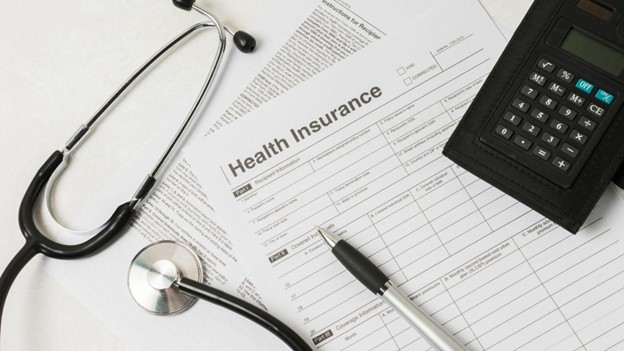 Health insurance claim forms with stethoscope, pen, and calculator on a desk, symbolizing the rising cost pressures in healthcare and medical billing.