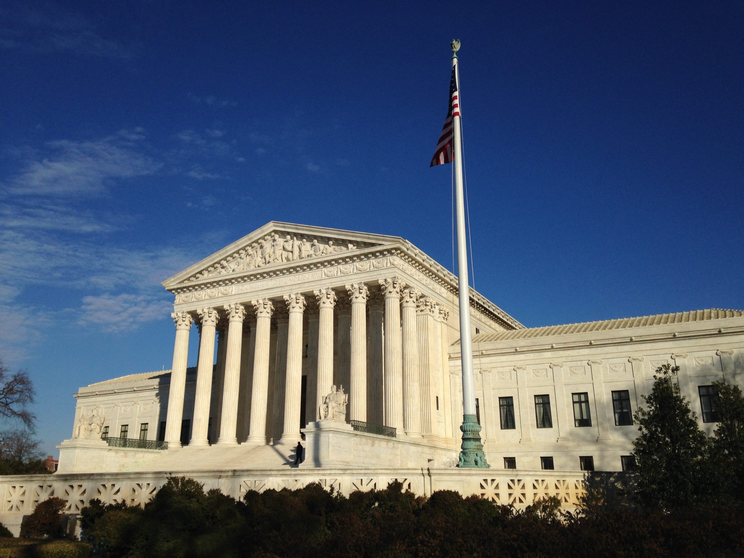 U.S. Supreme Court building with columns, American flag, and dramatic blue sky symbolizing legal authority and trade rulings.