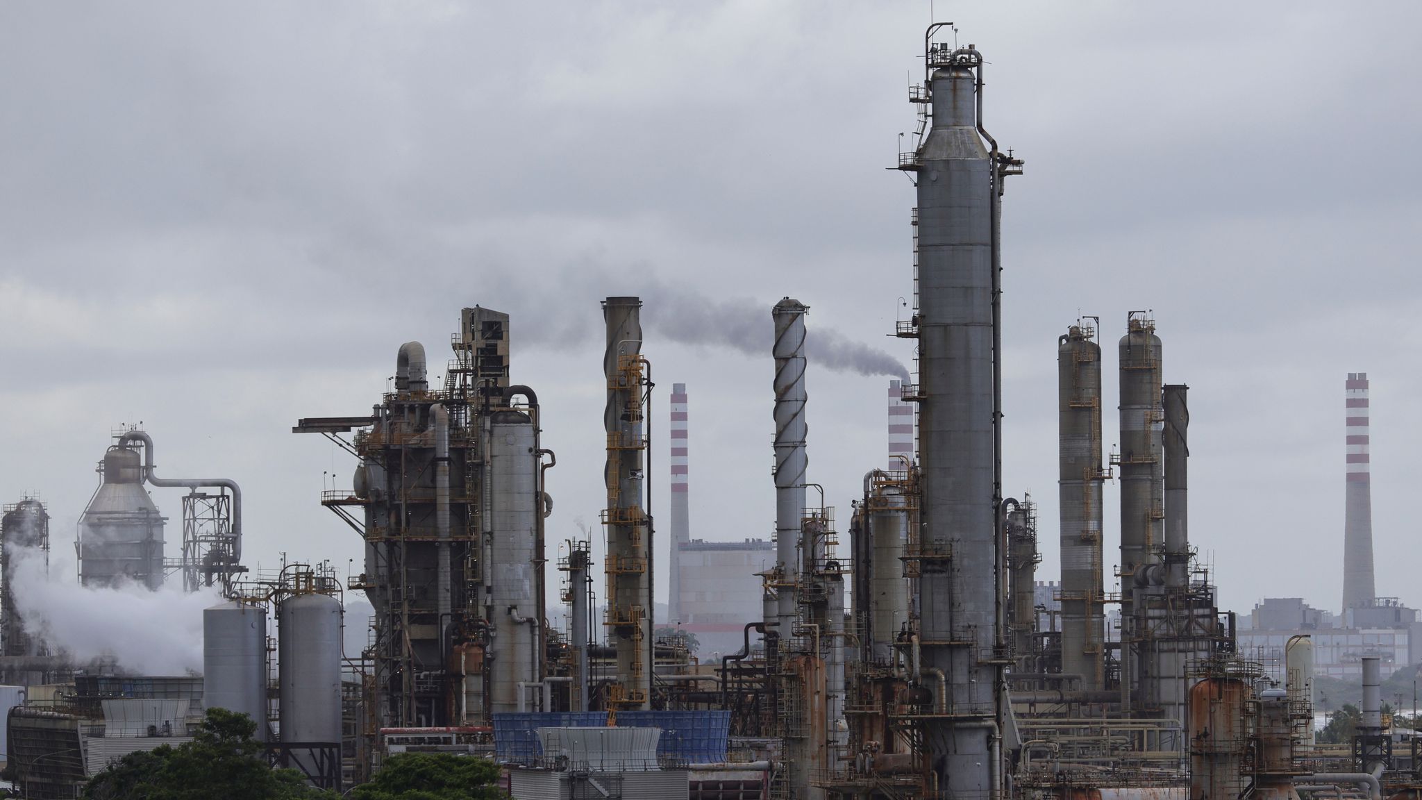 Venezuela offshore oil refinery infrastructure showing industrial decay, smoke emissions, and non-operational processing capacity, highlighting reconstruction investment risk.