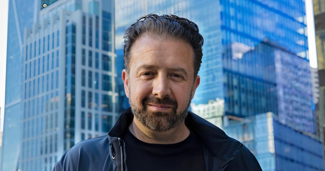 A technology executive stands outdoors in front of modern office buildings in a city business district