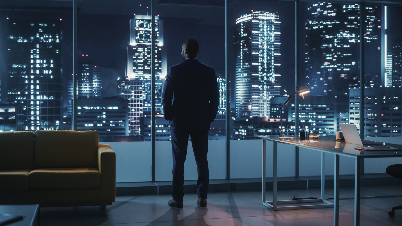 night office: successful black businessman wearing suit standing, looking out of the window on a big city. african american ceo thinking of environmental, social, corporate governance for e business
