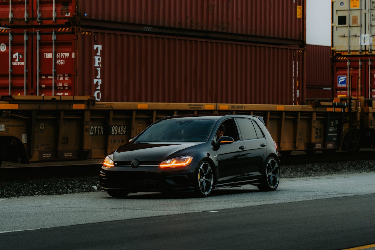 A black golf r is parked in front of a train